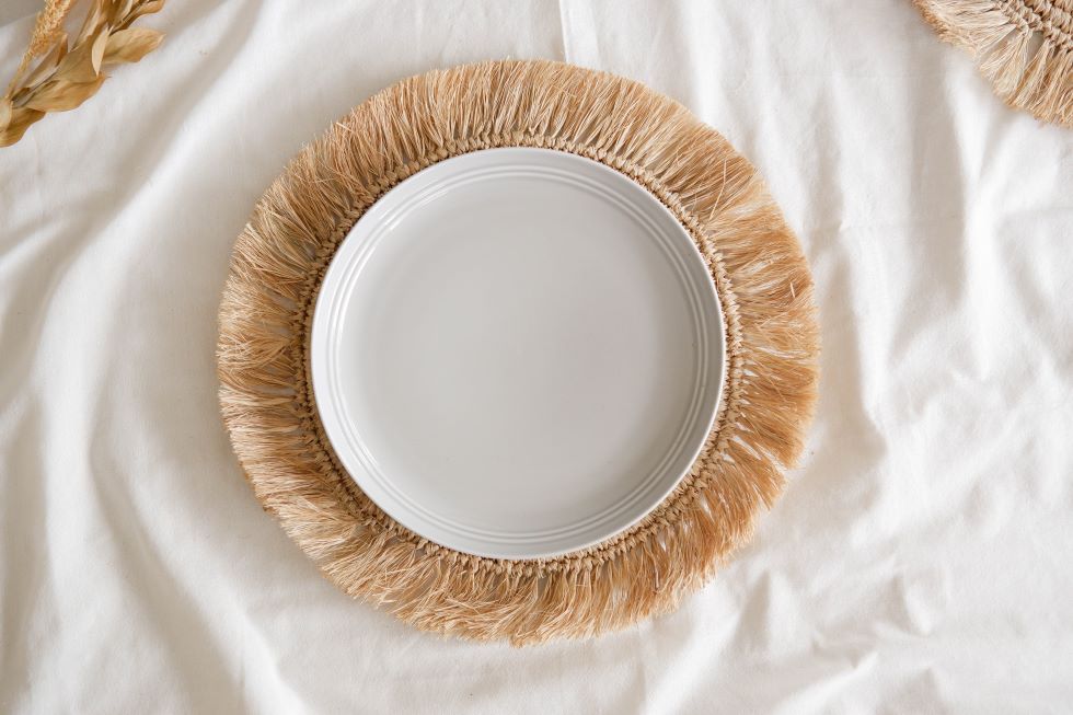 Boho-style raffia placemat with fringe edges, handcrafted from sustainable materials, perfect for coastal or earthy table settings